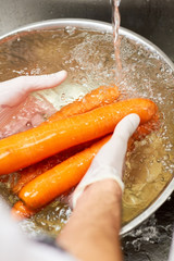 Several carrots washing under running water. Washing carrots in water with bubbles in metal bowl.