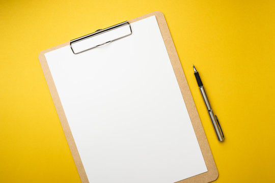 Wood clipboard with empty white paper and pen isolated on yellow background