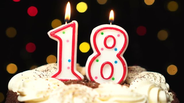 Number 18 on top of cake - eighteen birthday candle burning - blow out at the end. Color blurred background