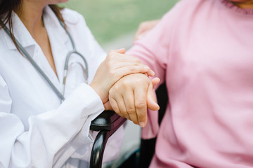 Closeup of an senior elderly woman's hand being held by a doctor while sitting on wheelchair, focus on hands