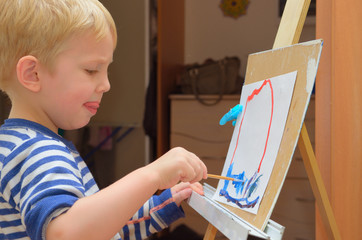 A little boy paints on an easel at home.