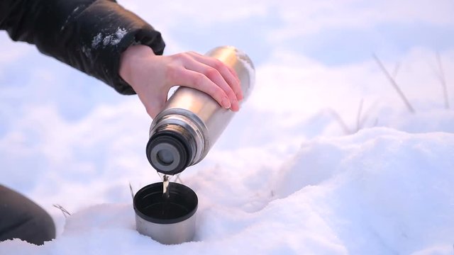 Metal thermos close up with female hand in snow