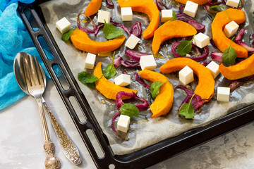 Baked pumpkin slices with onions, served with feta cheese, arugula and pumpkin seeds on a baking...