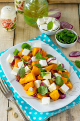 Warm pumpkin salad with onions, served with feta cheese, arugula and pumpkin seeds on a rustic table. The concept of healthy eating.