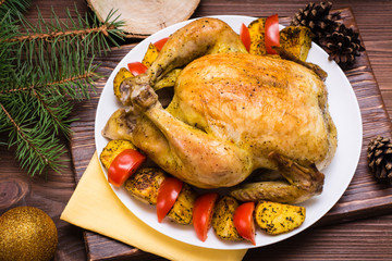 Baked whole chicken with a garnish of potatoes and tomatoes on a plate. Christmas decoration