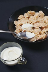 Traditional dish of dumplings in a bowl on a black tablecloth. Served with sour cream, a fork and a spoon.