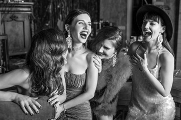 Group of young laughing stylish girls dressed classical style in interior of luxury club. Black-white photo.