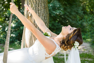 The bride ride a rope swing in the garden. Wedding in the forest.