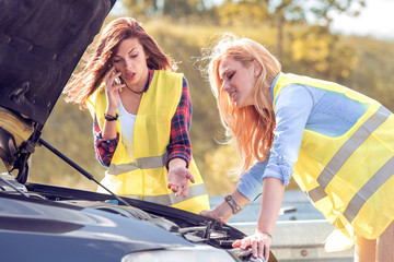 Two young girls with a broken car on the road.