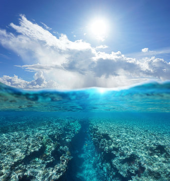 Over and under water surface seascape, sunlight with cloudy blue sky and split by waterline a natural trench in the reef underwater, Pacific ocean, French Polynesia