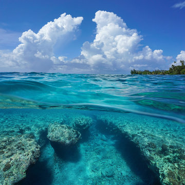 Seascape over and under sea surface, cloudy blue sky with a rocky seabed underwater split by waterline, outer reef of Huahine island, Pacific ocean, French Polynesia