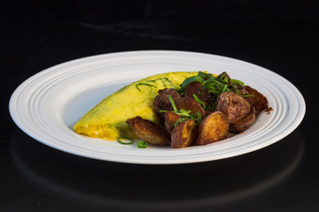French omelet with crispy home fries and green onions on a white plate.