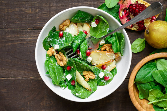 salad with spinach leaves, pear, nuts, pomegranate and feta cheese in a bowl with fork