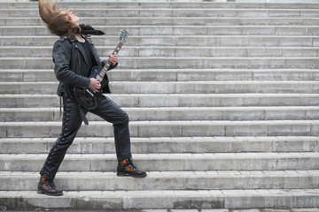 Fototapeta na wymiar Rock guitarist on the steps. A musician with a bass guitar in a 