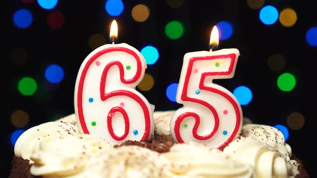 Number 65 on top of cake - sixty five birthday candle burning - blow out at the end. Color blurred background