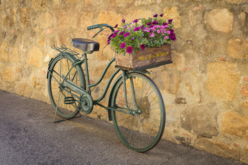 Fototapeta na wymiar style bicycle with box with flowers near the old wall in Tuscany city in Italy
