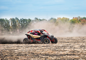 Fototapeta na wymiar Quad bike with two pilots in thick dust rides on plowed field