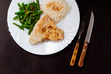 Turkey steak with green beans and rice on a black textured background.