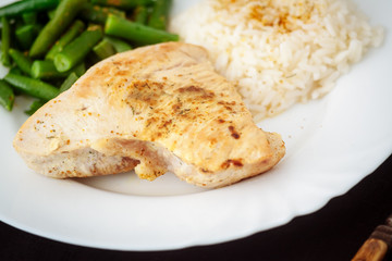Turkey steak with green beans and rice on a black textured background.