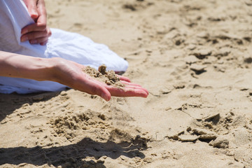 Woman holding sand in the hand on the beach, side view.