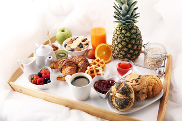breakfast in bed with fruits and pastries on a tray -waffles, croissants, coffe and juice