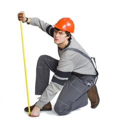 A young man in working grey clothes and orange hard helmet measuring the metric area in the room.