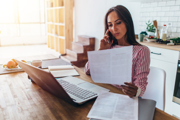 Woman using laptop and talking on mobile phone in kitchen