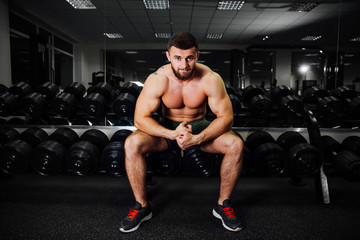 Fototapeta na wymiar bearded young bodybuilder sits on a stack with dumbbells. Rest between exercises.