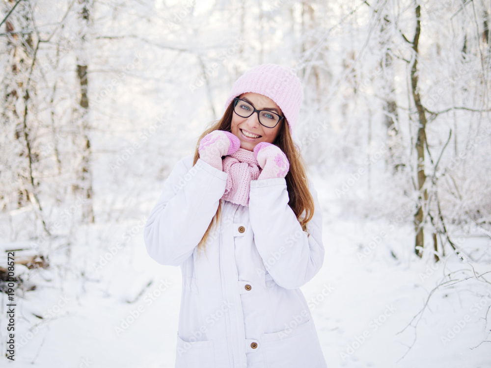 Wall mural Adorable happy young blonde woman in pink knitted hat scarf having fun strolling snowy winter forest in nature