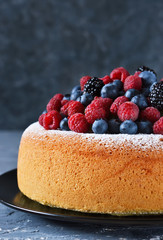 Vanilla cake with creamy cream and berries: blueberries, raspberries and blackberries on a concrete background.