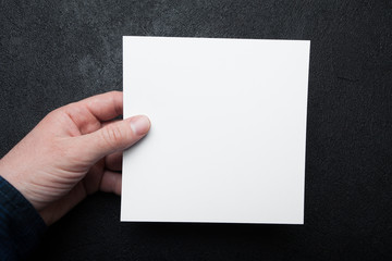 A square paper layout in a man's hand on a black vintage background.