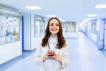 Plakat portrait beautiful girl doctor looking into the phone. Medical student wearing glasses at university background