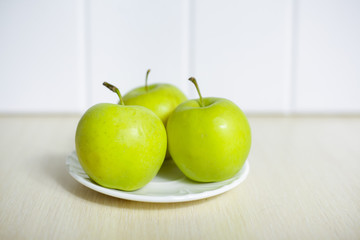 Green apples on a plate on a wooden table.
