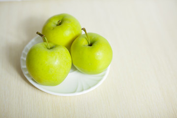 Green apples on a plate on a wooden table.