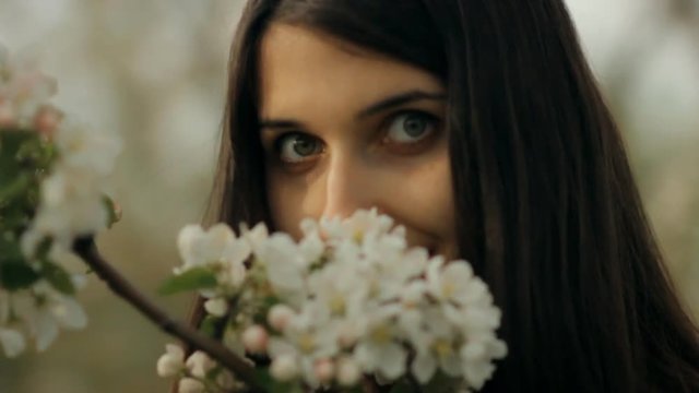 A young charming girl walks in the Park and enjoys the scent of blooming apple trees.