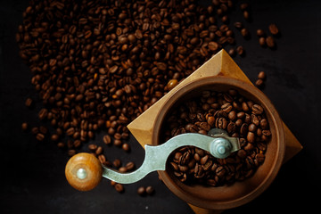 Coffee beans and an old hand grinder on a black textured background.