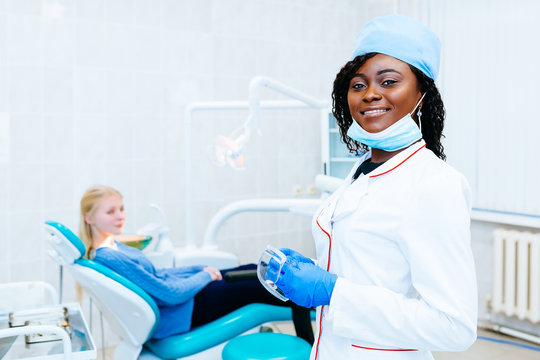 Young smiling African american female dentist in front of patient at clinic. Dental clinic concept.