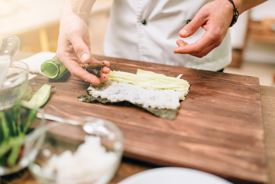 Male cook making sushi on wooden table, seafood