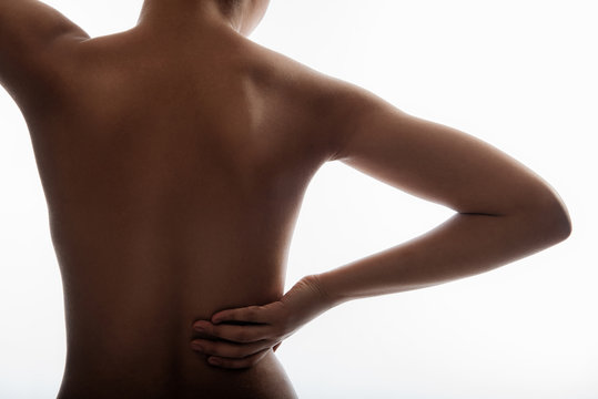 Close up of woman feeling pain in her back standing nude. Her skin is smooth. Isolated on background