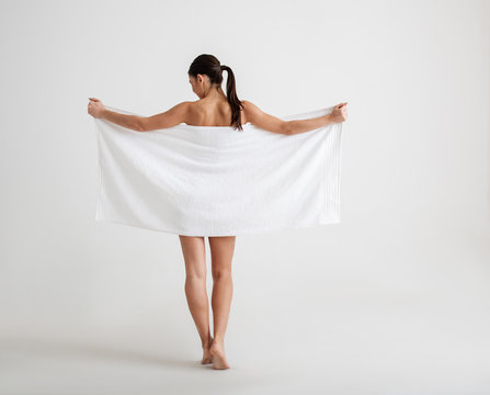 Undressed calm girl standing with her back. She is hiding her graceful body behind  a towel. Isolated on background Stock Photo | Adobe Stock
