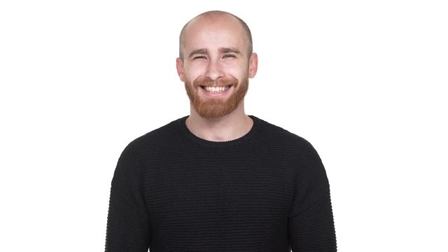 Portrait of cheerful manly man with shaved head smiling broadly on camera, being isolated over white background in studio. Concept of emotions