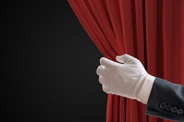 Actor is pulling red curtains in theatre with hand.