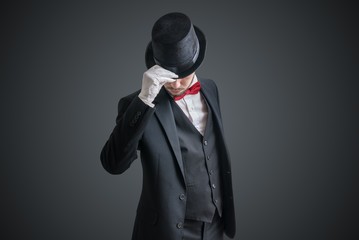 Gallant magician or illusionist in suit is taking off his hat.