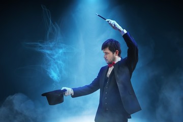 Magician or illusionist is showing magic trick. Blue stage light in background. - obrazy, fototapety, plakaty