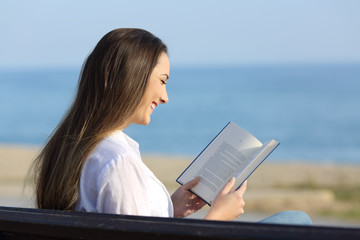 Woman reading a book sitting on a bench on the beach