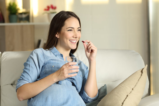 Happy pregnant woman taking a pill at home