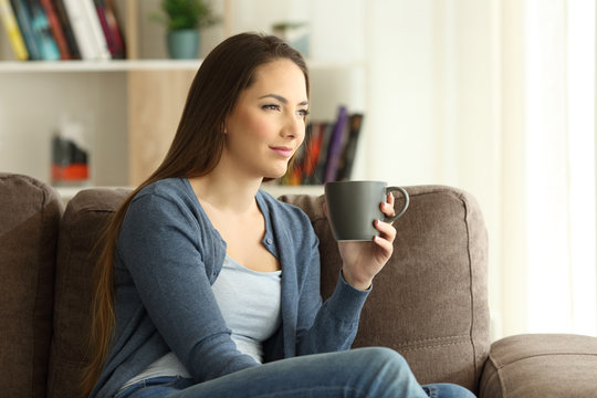 Woman drinking coffee and looking away on a couch