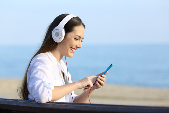 Woman listening to music sitting on a bench on the beach