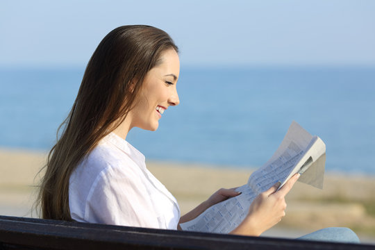 Woman reading a newspaper sitting on a bench on the beach