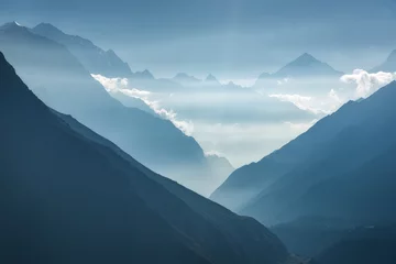 Papier Peint photo Himalaya Vue majestueuse des silhouettes des montagnes et des nuages bas au coucher du soleil au Népal. Paysage avec de hauts rochers de montagnes himalayennes, un beau ciel bleu et des rayons de soleil. Himalaya incroyable. Fond de nature